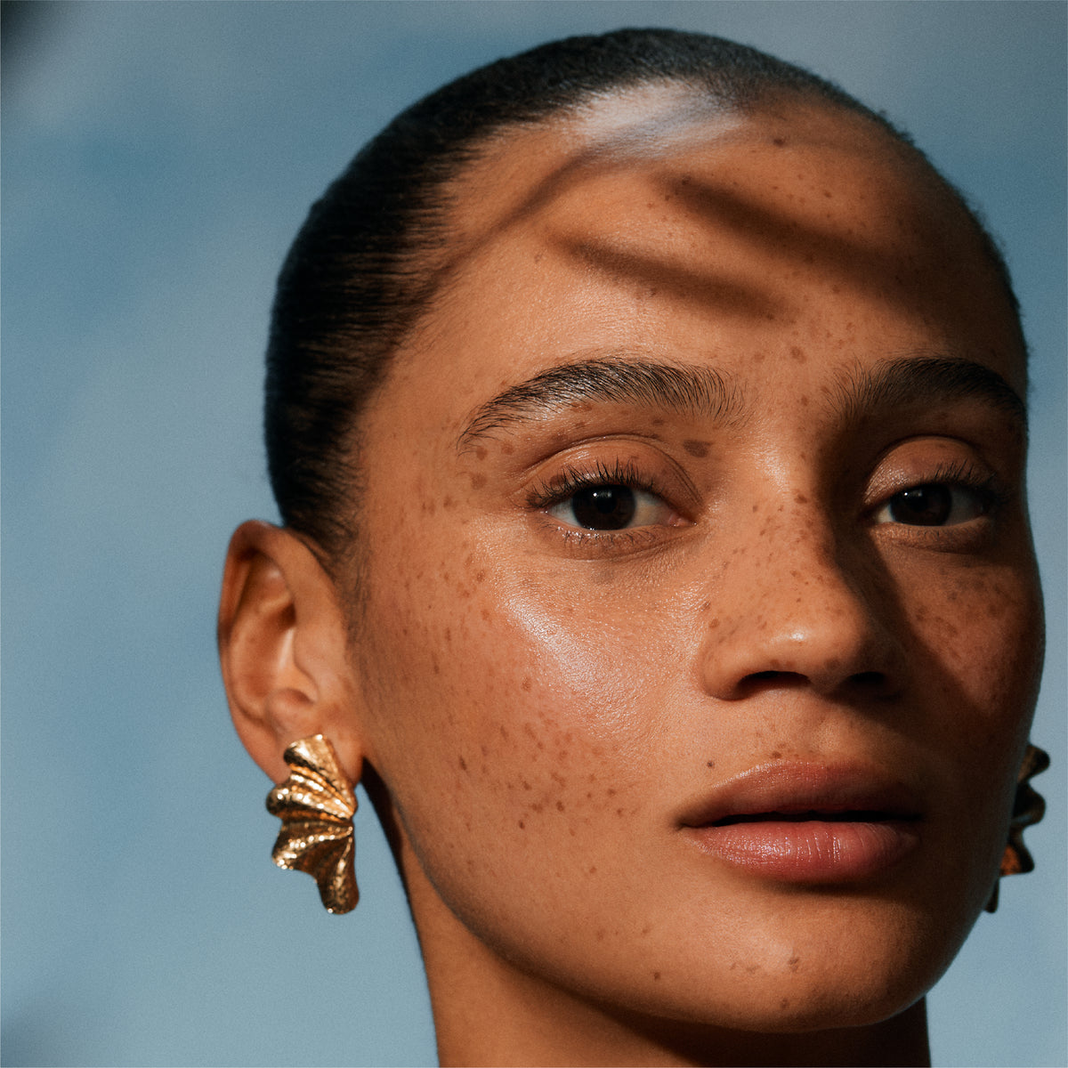 Close-up of a person wearing gold earrings against a blue background