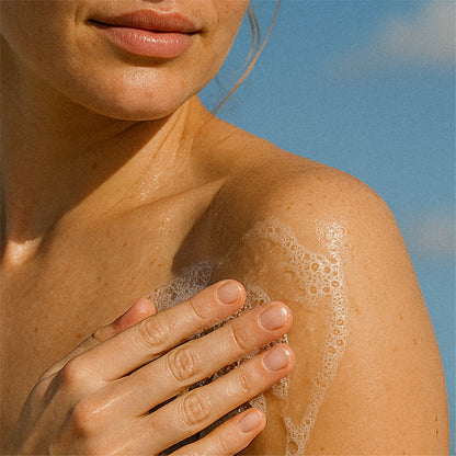 Person applying Irene Forte Apricot Body Wash to their shoulder with a blue sky background